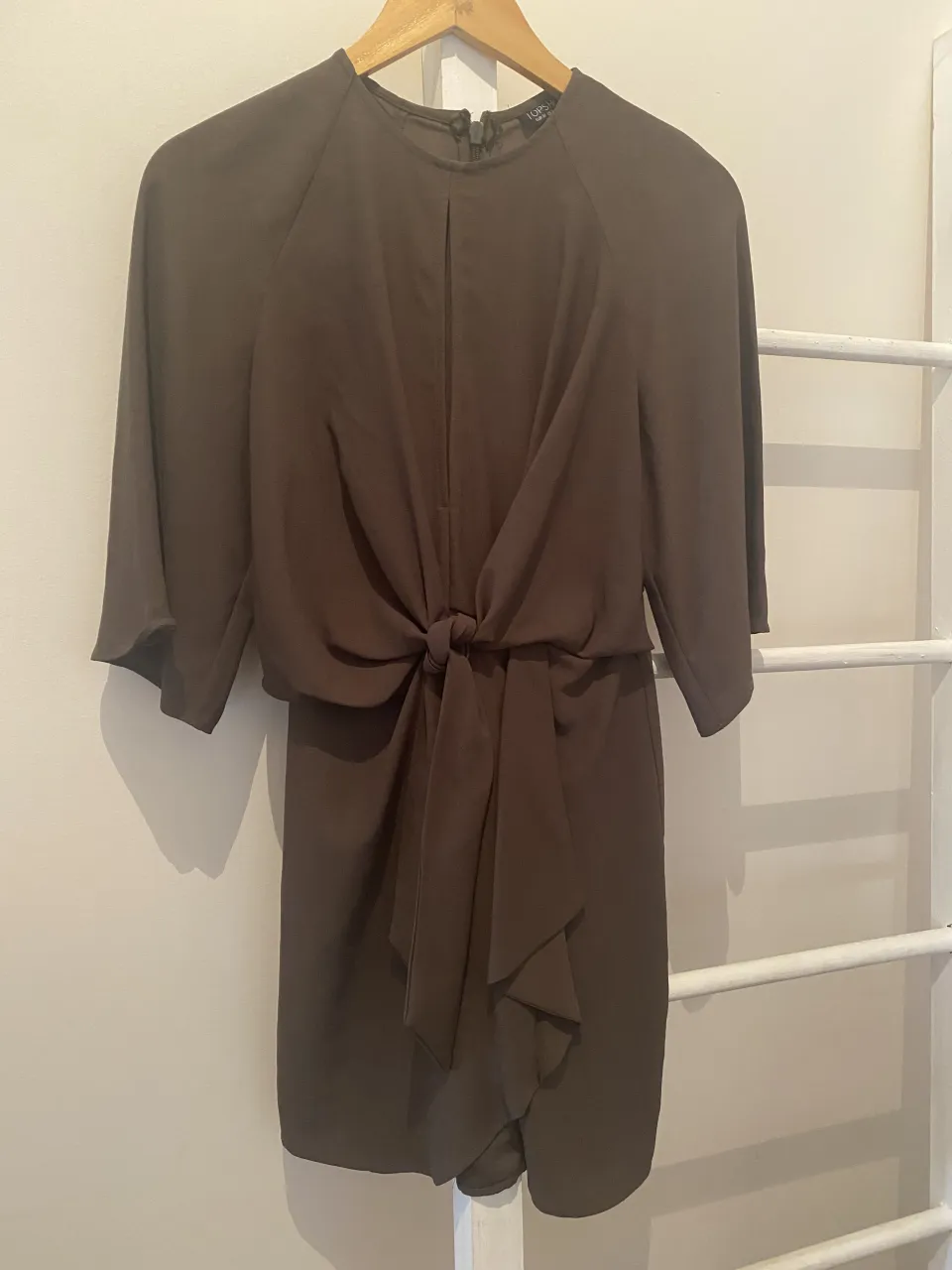 Vestido corto de crepé color verde militar, con mangas 3/4 y detalle de lazo en la cintura. Ideal para un look elegante y moderno.