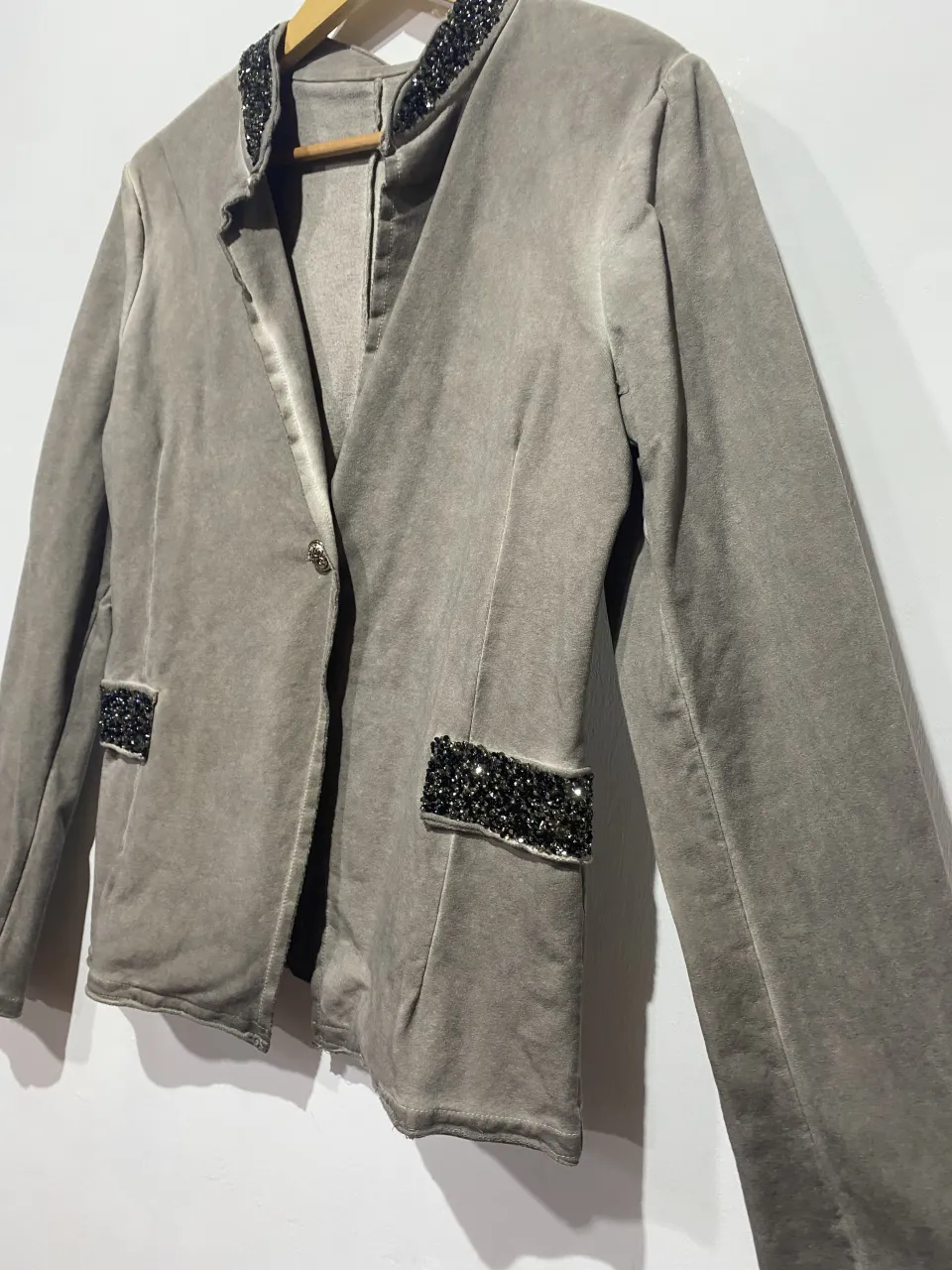 Blazer gris con detalles de pedrería en cuello y bolsillos. Posee un solo botón al frente y un corte moderno.