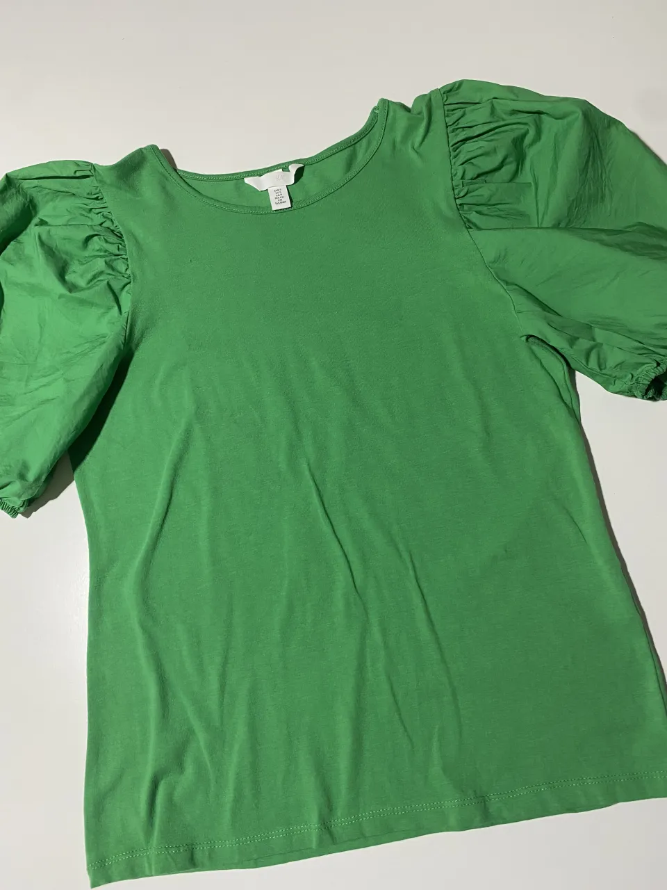 Remera verde con mangas abullonadas y detalles fruncidos en los hombros y puños. Un diseño moderno y femenino, ideal para un look casual y chic.