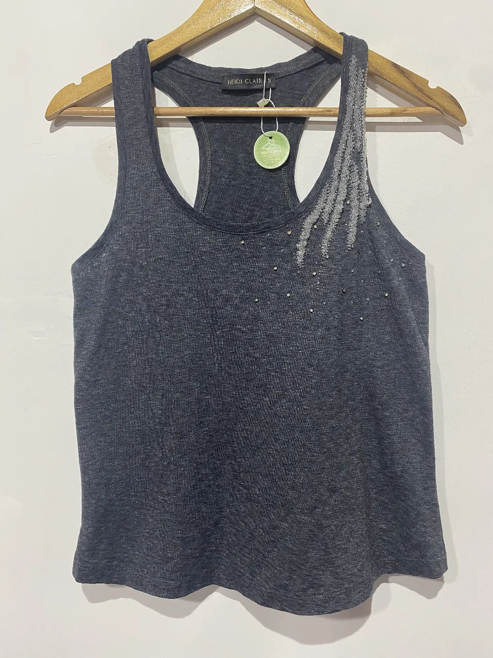 Musculosa gris oscuro con detalles de strass y mostacillas en la parte delantera superior. Diseño moderno y canchero, ideal para un look casual o para entrenar con estilo.