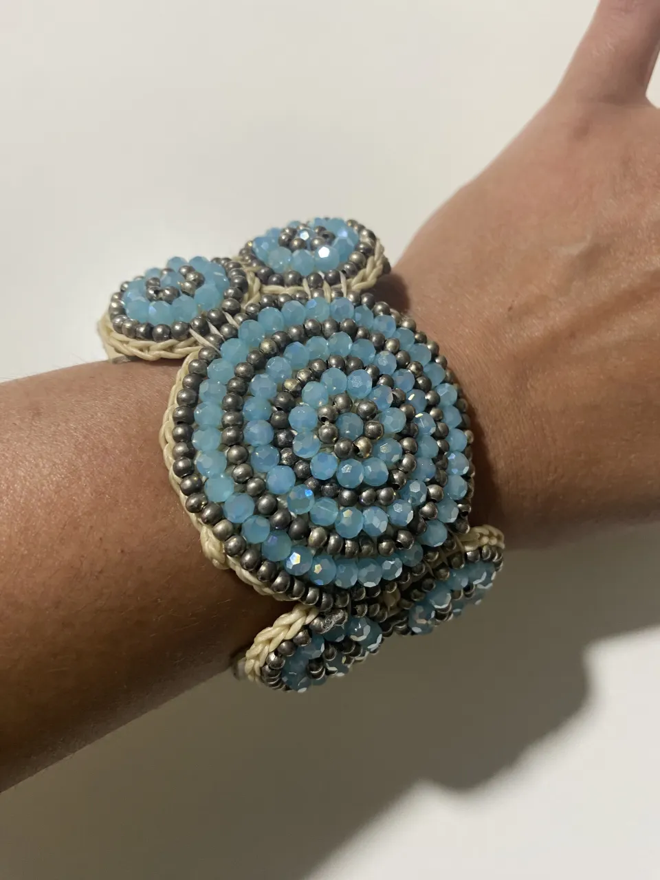 Pulsera ancha de cuero con apliques de mostacillas y cristales celestes en forma de espiral y círculos. Cierre de broches.