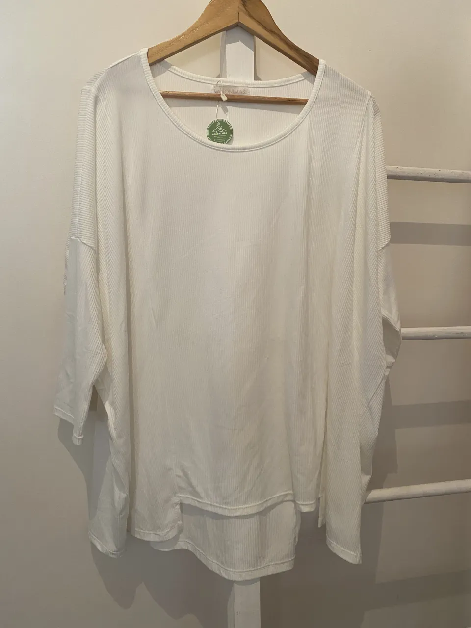 Remera blanca de manga larga, con cuello redondo y un corte holgado. Su tejido acanalado le da un toque moderno y cómodo, ideal para el día a día.