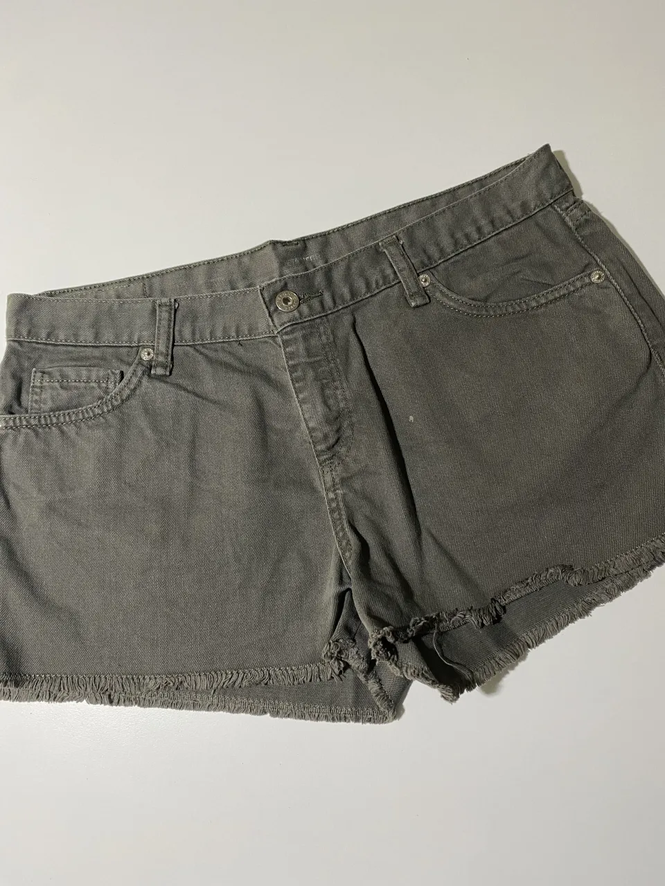 Shorts de jean grises con roturas y detalles deshilachados en los bordes. Tiro alto, con bolsillos y cierre.