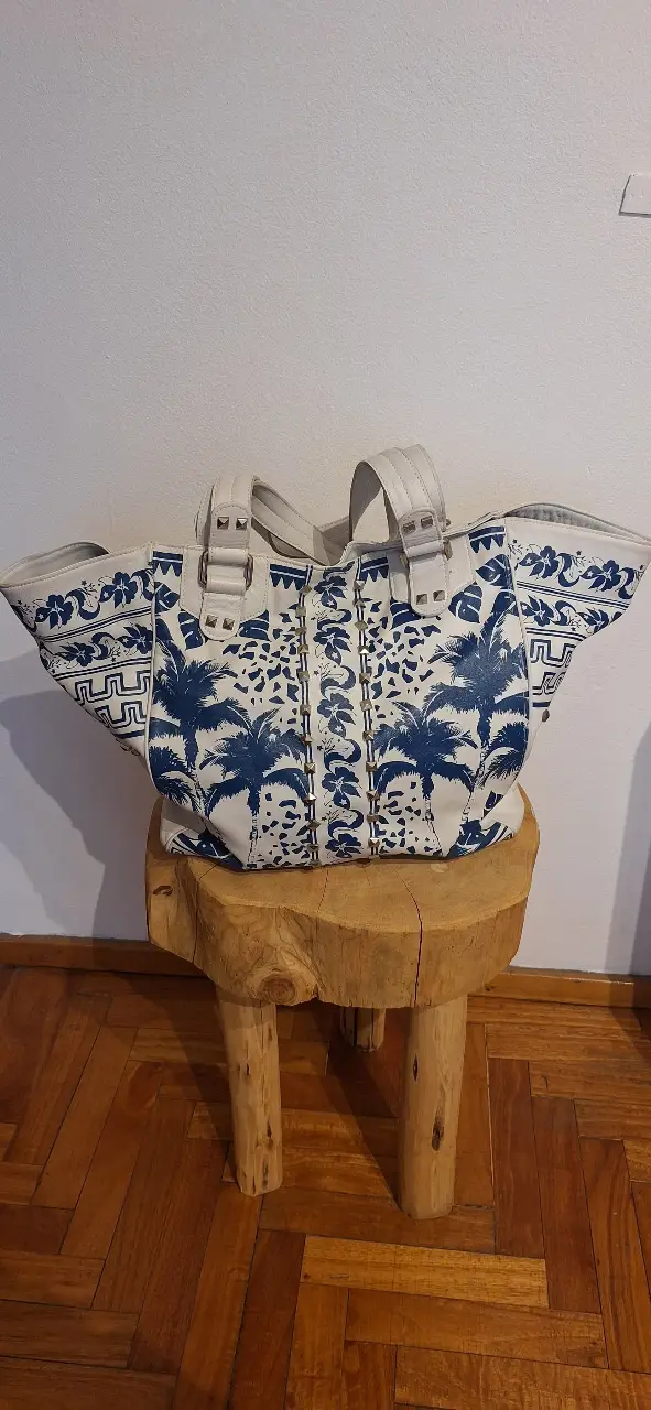 Cartera tote bag de cuero vacuno con estampado floral en azul y detalles de tachas. Interior con forro de algodón y bolsillo con cierre. Ideal para un look casual y con estilo.