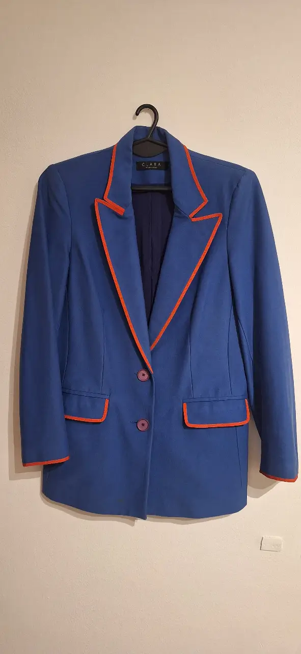 Blazer azul con detalles en naranja. Corte clásico con solapas y bolsillos. Ideal para un look elegante y moderno.