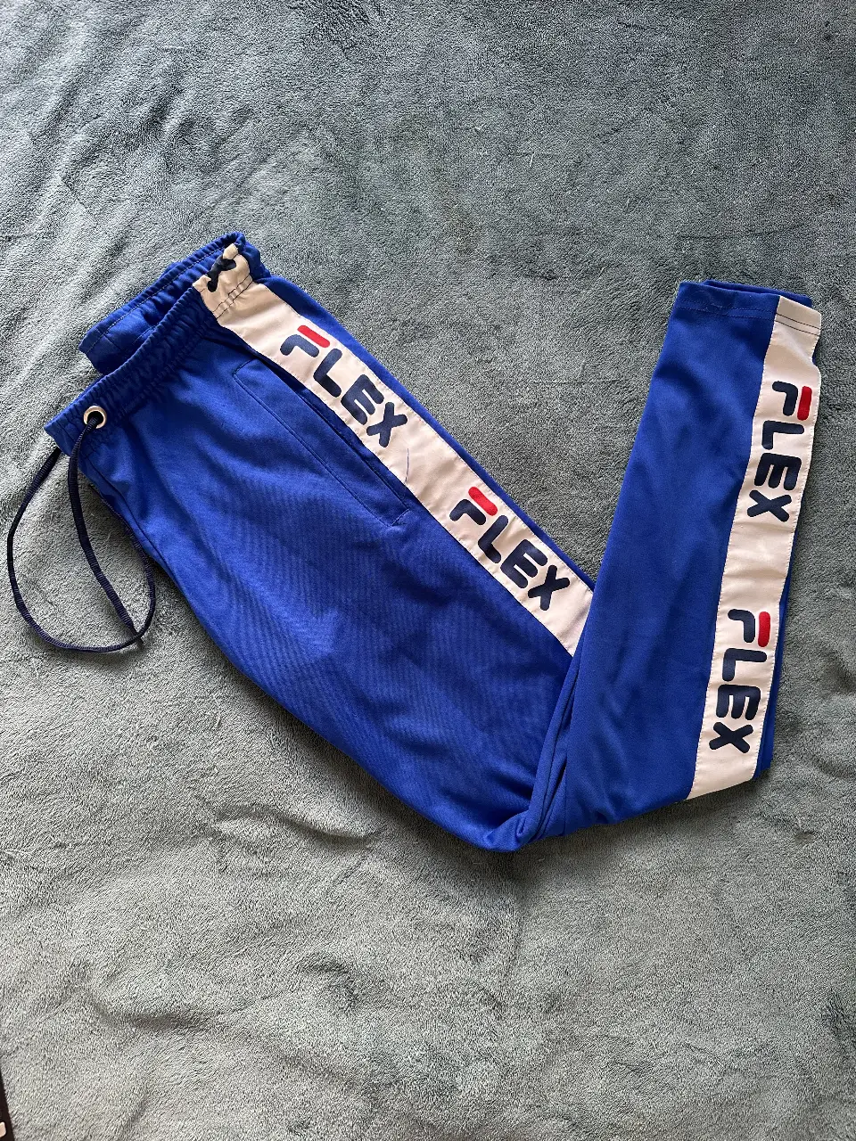 Pantalón deportivo azul con detalles en blanco y rojo. Estilo "Flex" con ajuste suelto y cordón en la cintura. Ideal para un look casual y cómodo.