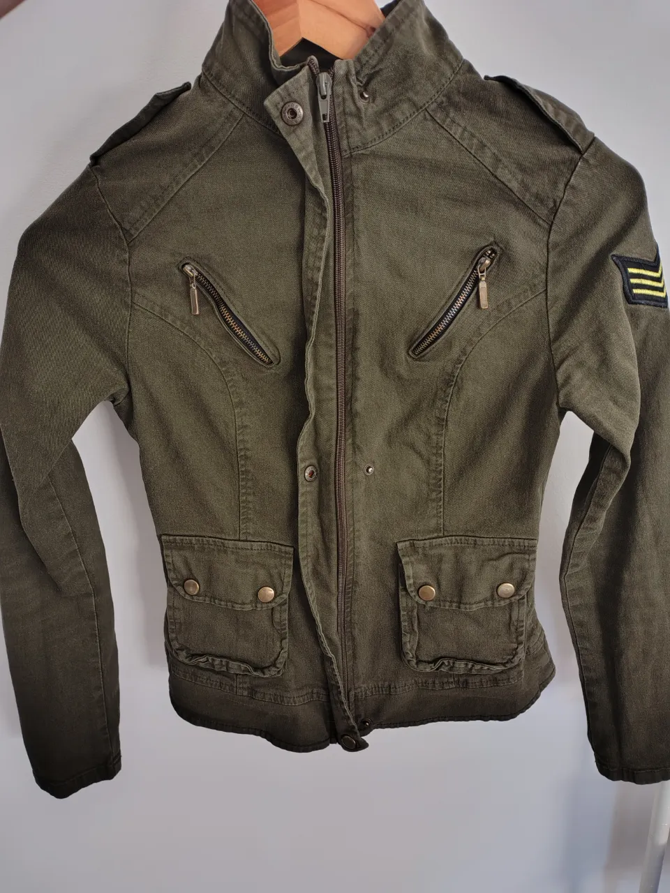 Campera de gabardina elastizada color verde militar con cuello mao, cierre al frente y bolsillos con tapa y botones. Posee detalles de cierres en los bolsillos superiores y parches con franjas amarillas y negras en las mangas.
Marca: Zamm
Talle: M
Cantidad de bolsillos externos: 2
Se encuentra en buen estado.