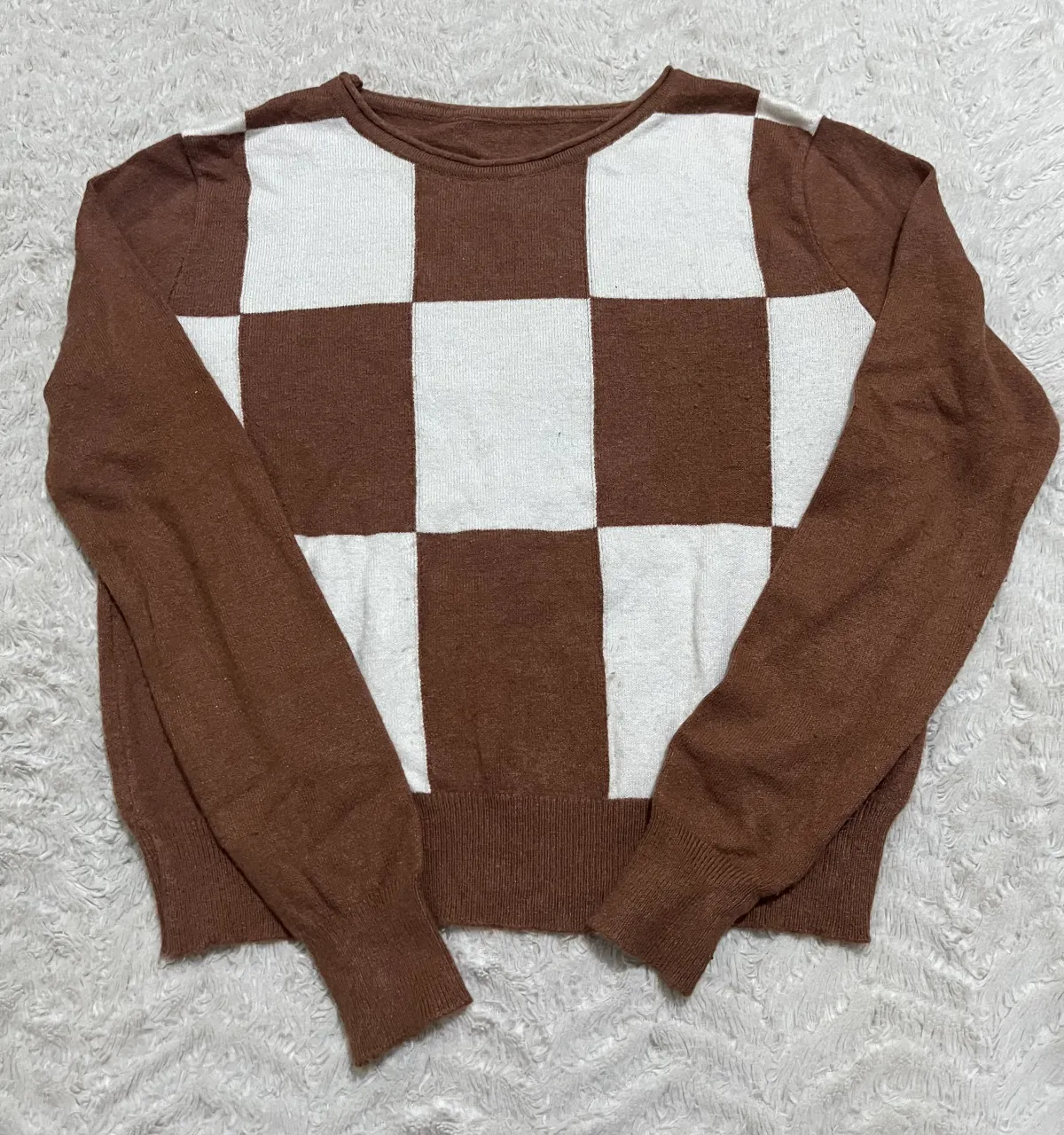 Sweater de manga larga con diseño de tablero de ajedrez en marrón y blanco. Cuello redondo y puños tejidos.