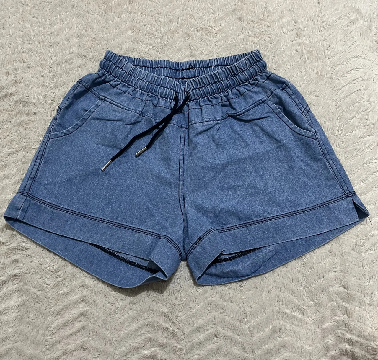 Shorts de jean color azul claro con cordón negro en la cintura. Posee bolsillos delanteros y detalles de costura.