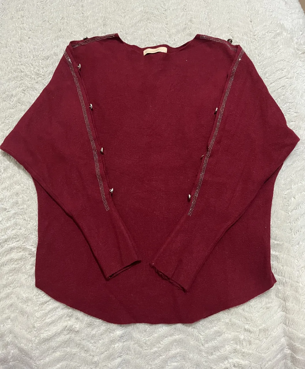 Sweater de manga larga color bordó con detalles de tachas plateadas a lo largo de los hombros y los puños. Escote en V.