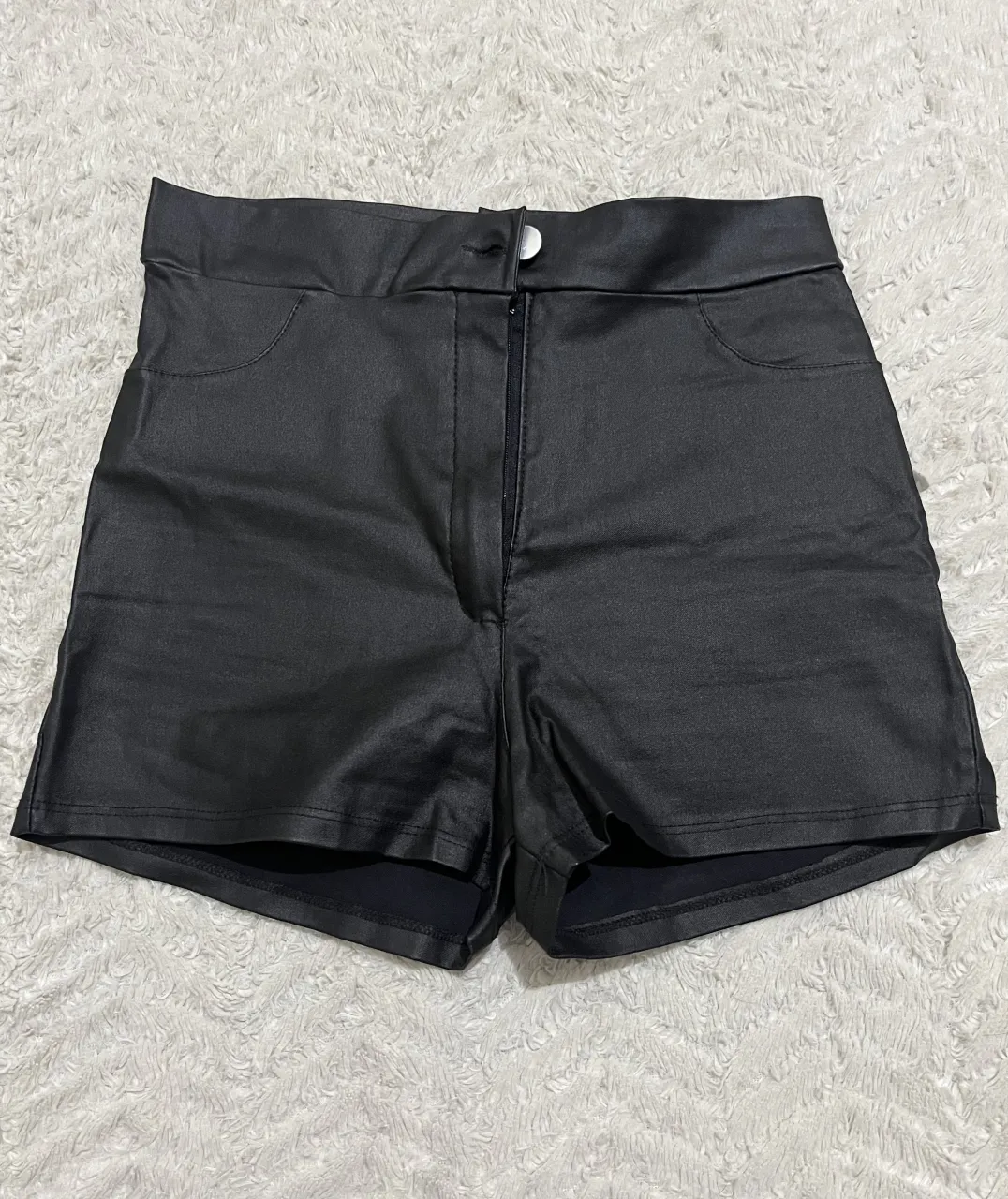 Shorts negros de cuero sintético con bolsillos delanteros y traseros. Cierre y un botón en la parte frontal.