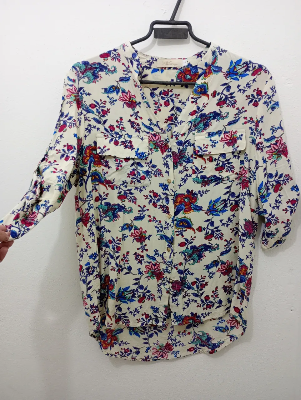 Camisa estampada con flores y pájaros en tonos vibrantes. Posee cuello escote en V, mangas 3/4 con detalle de puño y dos bolsillos en el frente. Ideal para un look casual y fresco.