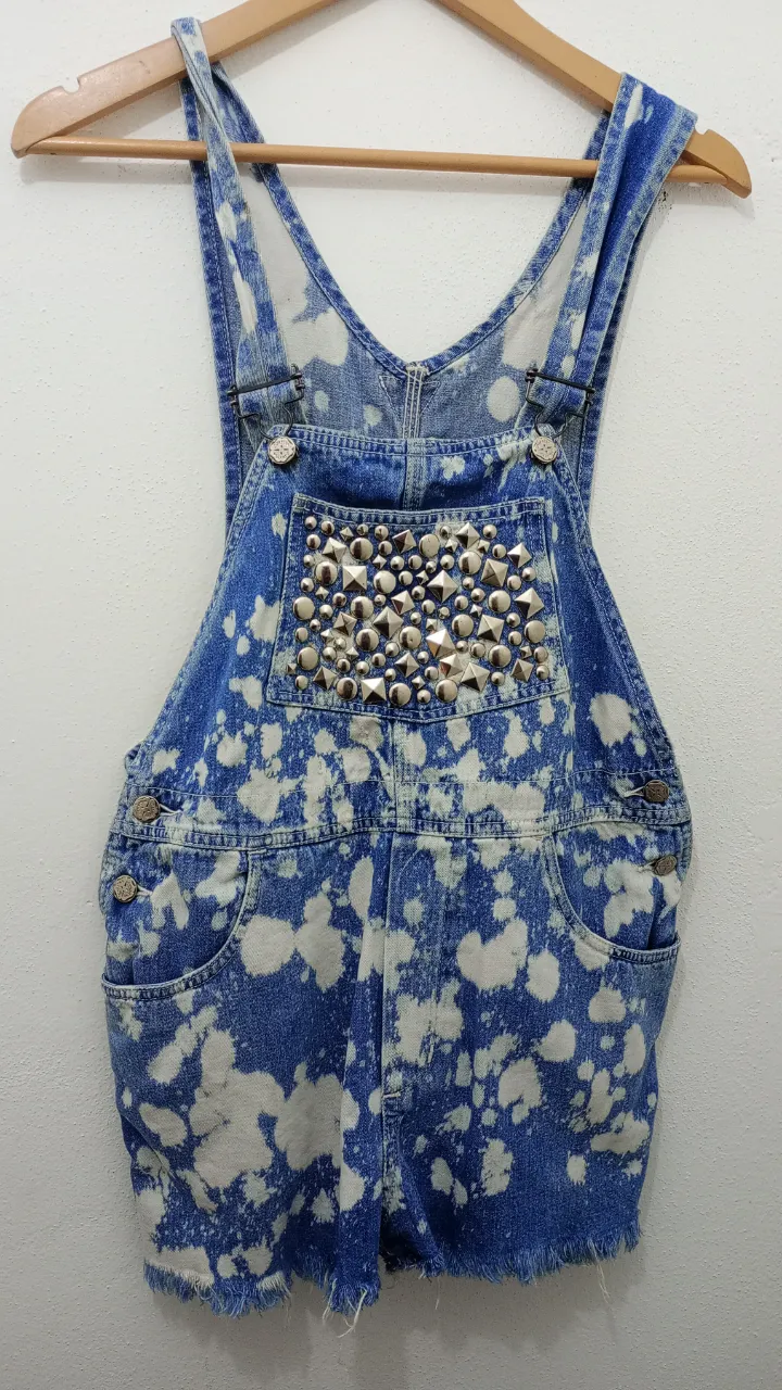 Shorts de jean tiro alto intervenidos con efecto tie-dye en blanco y azul. Tienen tachas plateadas en la parte delantera y ruedo deshilachado. ¡Un diseño único para destacar tu estilo!tiene unos pequeños detalles de óxido en su parte interior que no son visibles al usarlo pero aclaro detalles.