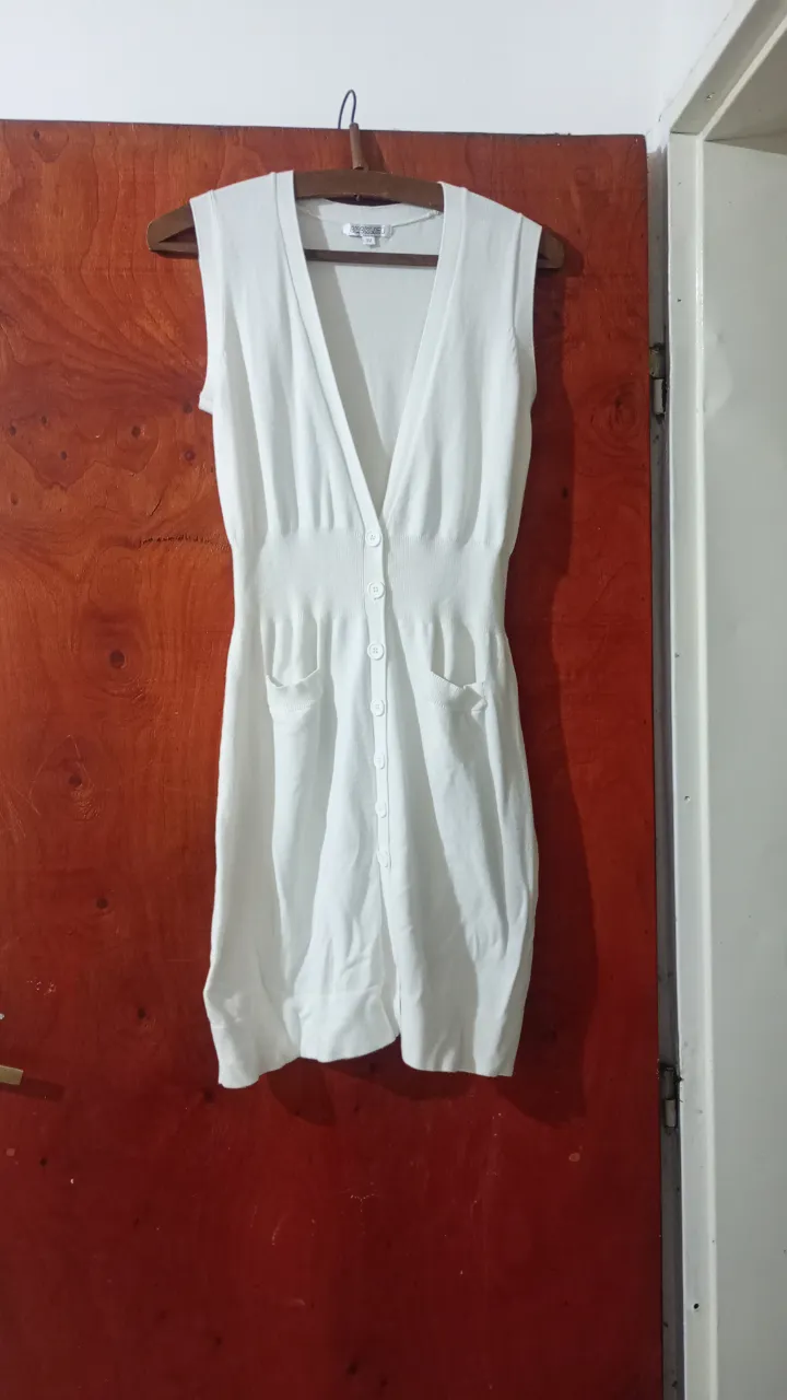 Vestido blanco sin mangas, con escote en V y botones al frente. Posee dos bolsillos aplicados en la parte inferior.