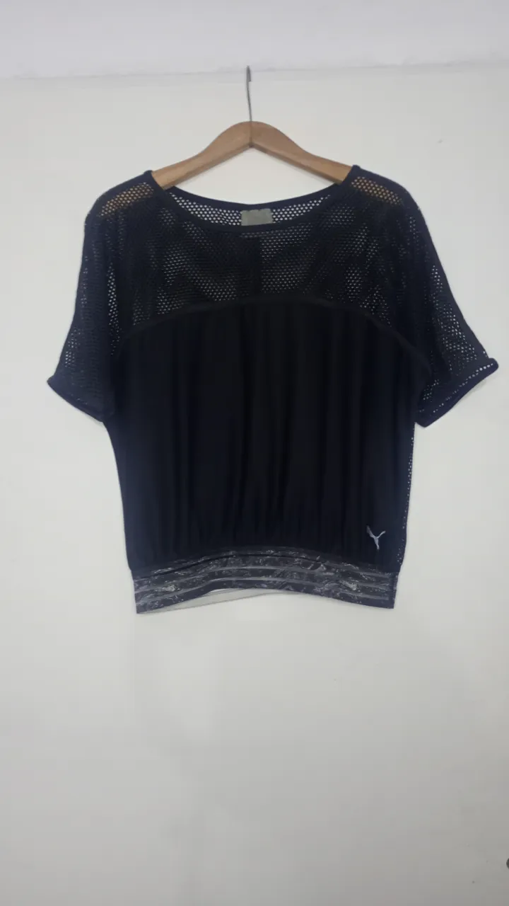 Remera deportiva negra de manga corta con detalles de red en la parte superior y mangas. Posee elástico en la cintura.