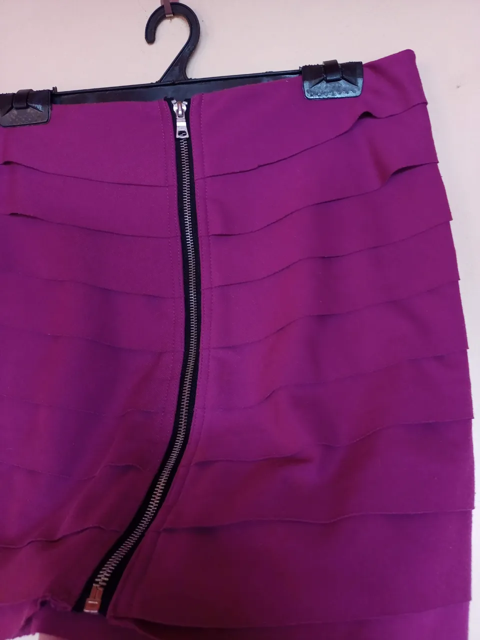 Pollera corta morada con cierre metálico asimétrico al frente y volados horizontales.