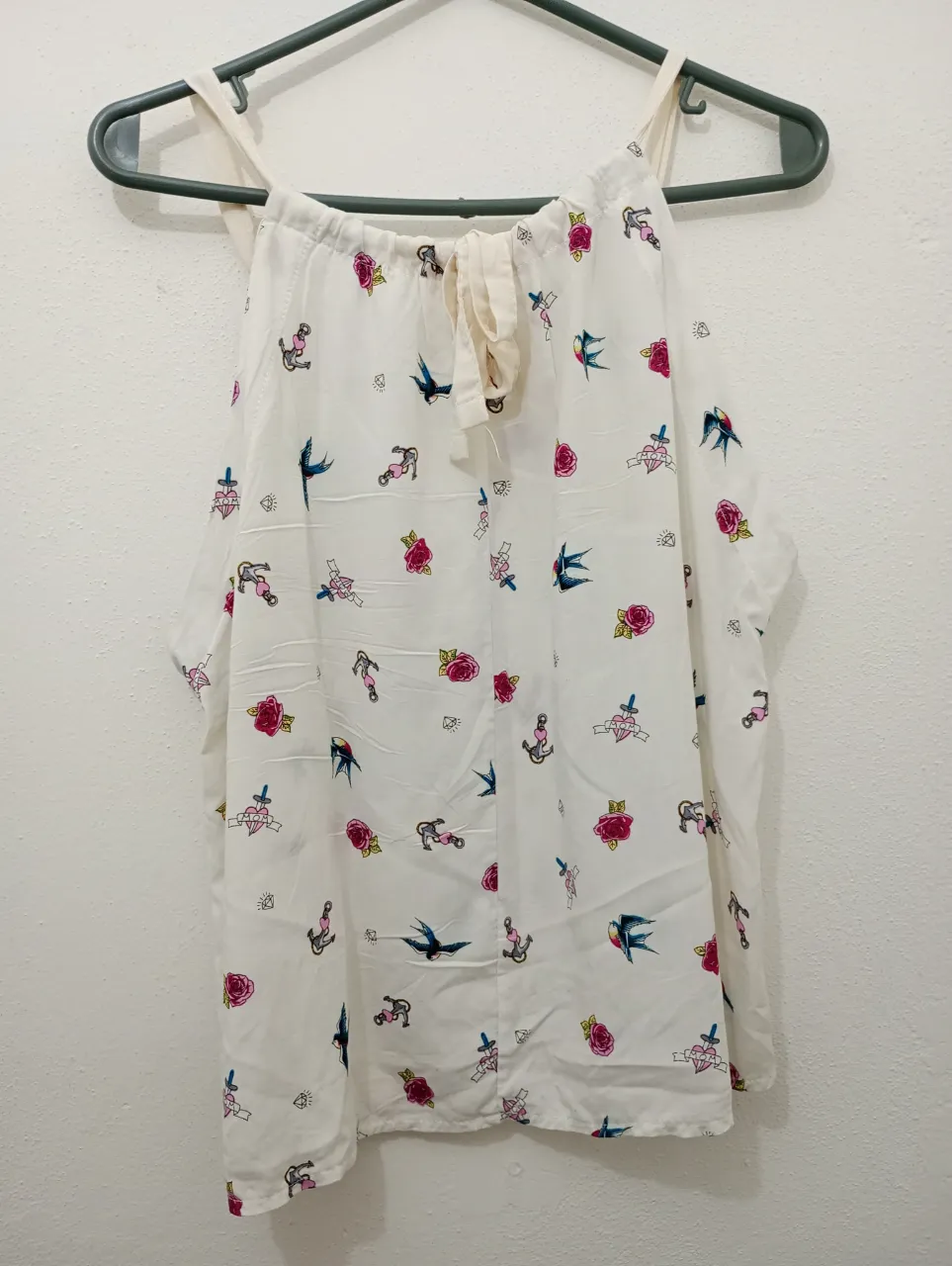 Musculosa blanca con estampa de "tatuajes" . Tiene un diseño súper original con golondrinas, rosas, anclas y corazones. El cuello es halter y tiene un detalle de lazo para atar. Ideal para un look canchero 