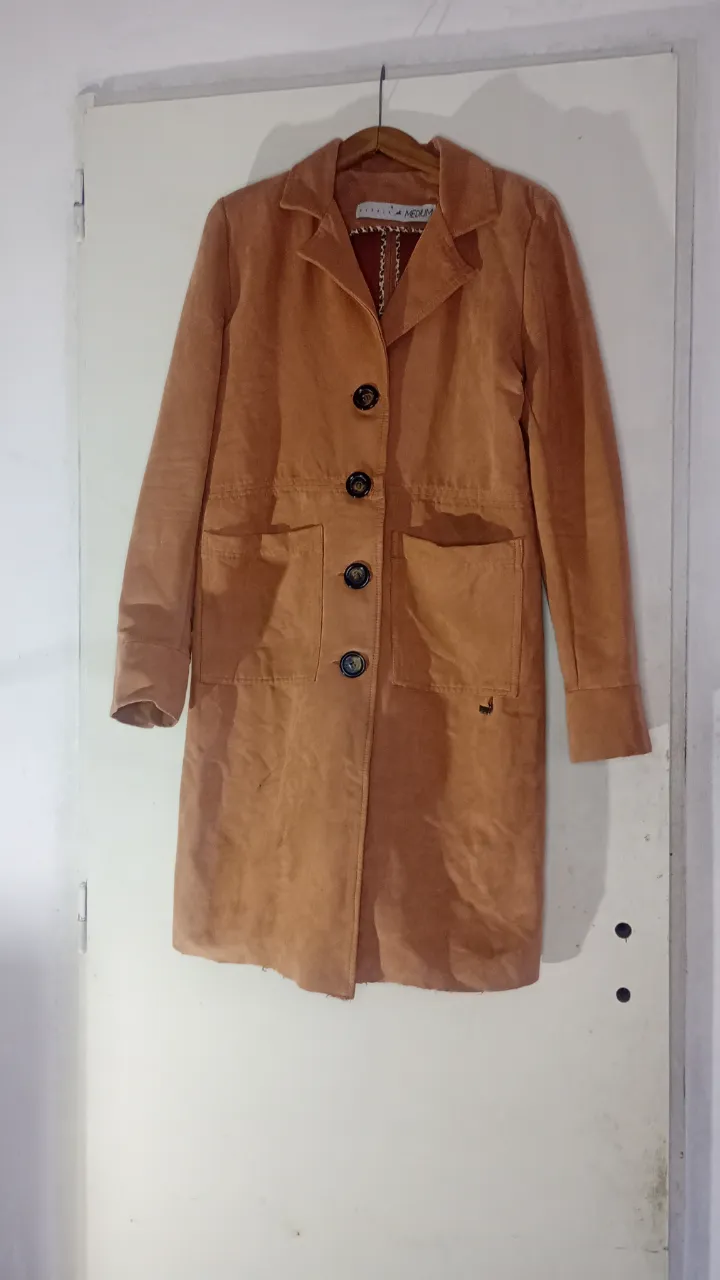 Tapado de piel de durazno color suela con cuello solapa, 4 botones al frente y dos bolsillos con tapa. Posee un detalle metálico con la marca en uno de los bolsillos. en la última foto se aprecia un detalle de una pequeña quemadura de sahumerio que tiene en la espalda a la altura casi del hombro 