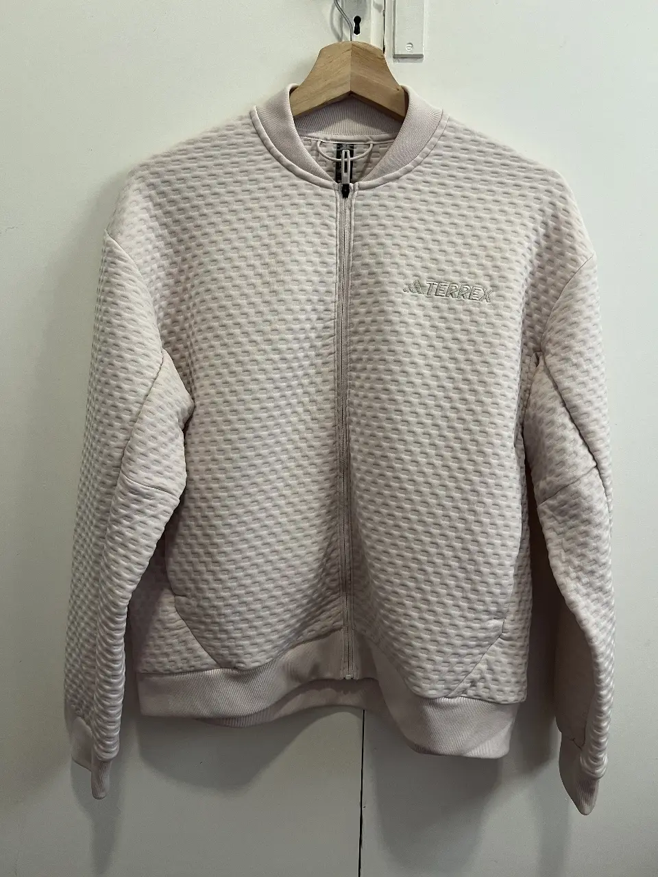 Campera bomber Adidas Terrex, color rosa claro con textura en relieve. Con cierre frontal, logo de la marca y puños y cintura elastizados. Ideal para un look deportivo y casual.