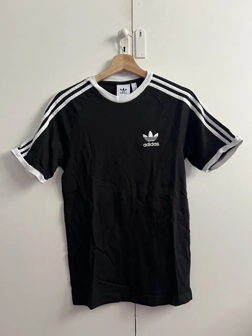 Remera Adidas Originals 3 Stripes, negra con las tres tiras blancas en las mangas y detalles blancos en el cuello y mangas. Logo Adidas bordado en blanco en el pecho. Ideal para un look deportivo y casual.