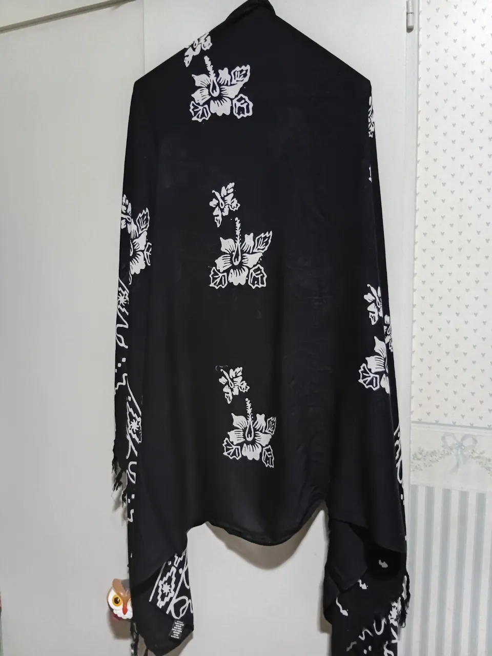 Pañuelo o chal negro con estampa de flores blancas estilo hawaiano. Tiene flecos en los bordes. Ideal para complementar outfits de playa o casuales.