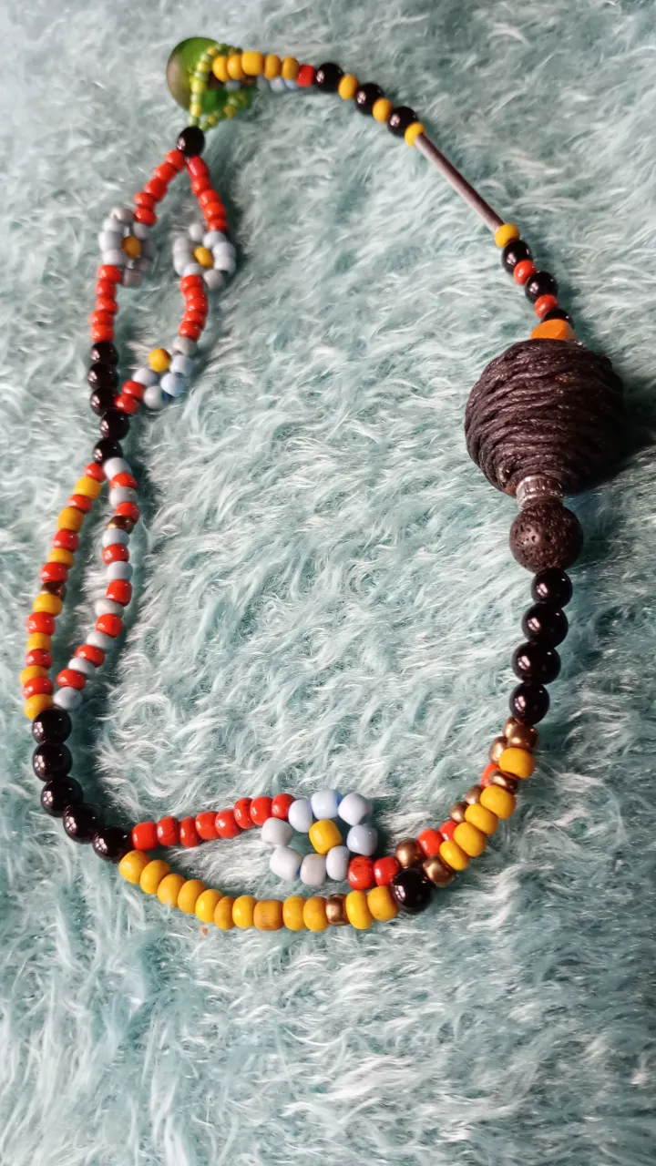 Collar Florcita, canchero y colorido, de mostacillones, con cuentas de madera, piedra volcánica  y bola de hilo de algodón.            
 Un accesorio único y llamativo, perfecto para darle un toque bohemio y original a tu look. Ideal para festivales, salidas casuales o para añadir un toque de color a tu día a día.
Mide 41cm