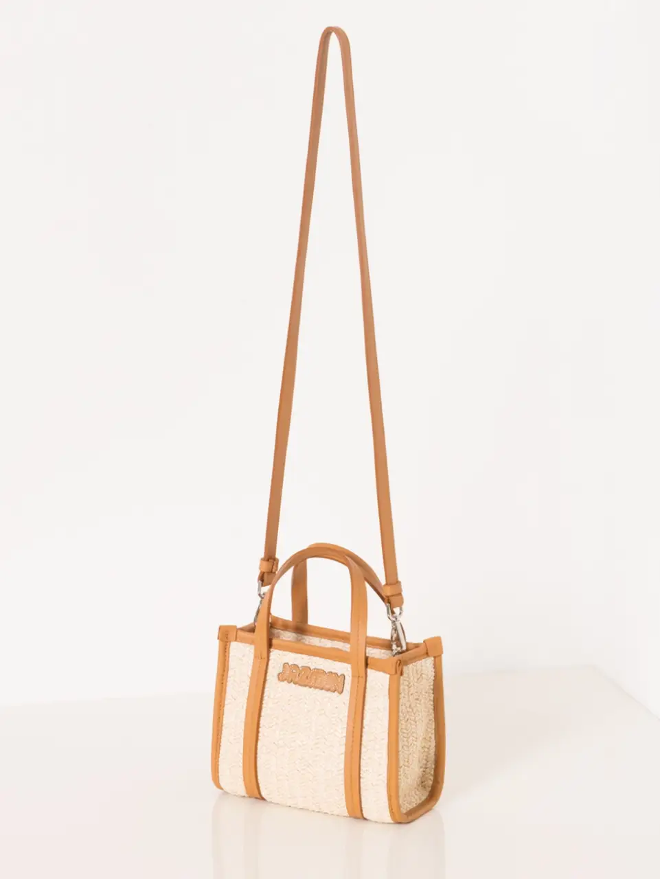 Cartera tipo tote bag de tela con detalles en cuero marrón. Ideal para llevar tus esenciales con estilo. Diseño con el nombre "JAZMIN" en relieve.