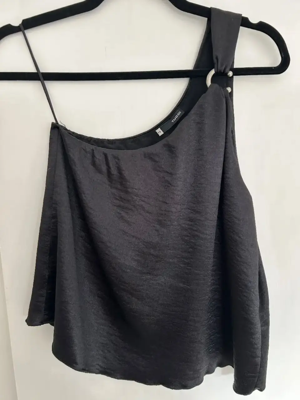 Top negro asimétrico de satén con detalle de aro metálico en el hombro. Ideal para una salida o evento especial.