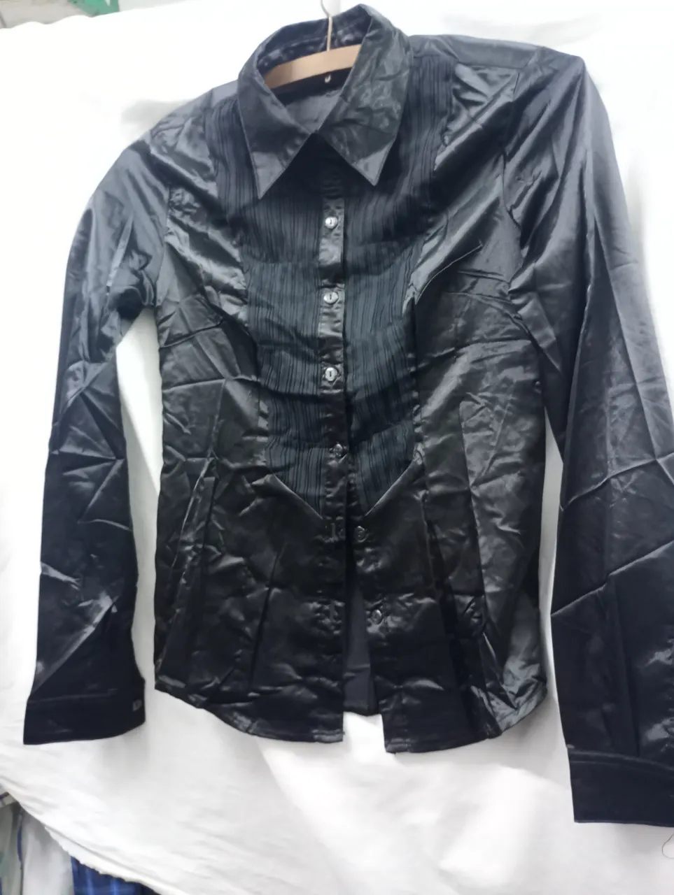 Camisa negra de manga larga con botones al frente y detalles de frunces verticales en el torso. Cuello camisero.