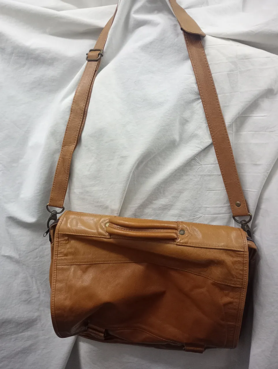 Bolso de cuero marrón, tipo mensajero, con correa regulable y manija superior. Posee múltiples compartimentos internos y externos, incluyendo bolsillos con cierre y ranuras para tarjetas. Ideal para el día a día, trabajo o salidas casuales.