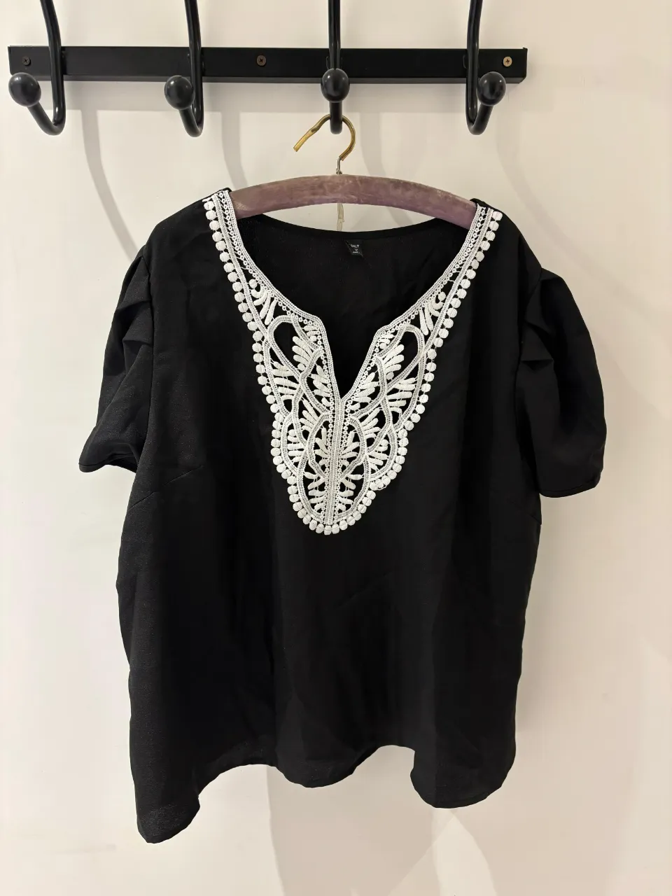 Remera negra con escote en V y detalles de bordado blanco en el cuello. Manga corta y corte holgado.