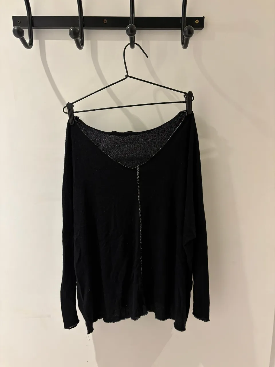 Sweater negro de manga larga con escote en V pronunciado. Posee costura central al frente y detalles sutiles en el cuello. Ideal para un look casual y cómodo.