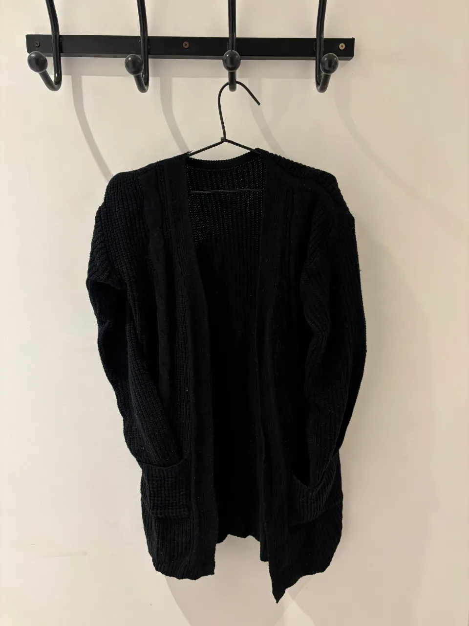 Cardigan negro de tejido grueso, con bolsillos frontales y mangas largas. Ideal para un look casual y abrigado.