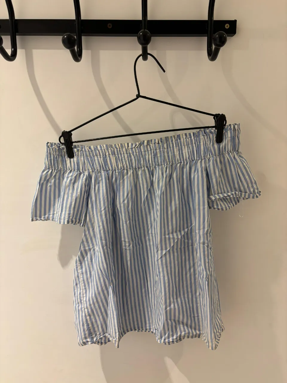 Remera a rayas celestes y blancas, con hombros descubiertos y mangas cortas con volados. Ideal para un look fresco y casual de verano.