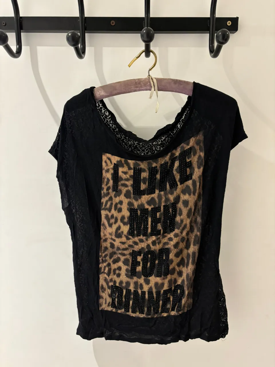 Remera negra con estampa "I LIKE MEN FOR DINNER" y detalles de animal print y strass. Posee detalles de encaje en mangas y cuello. Ideal para un look canchero y audaz.