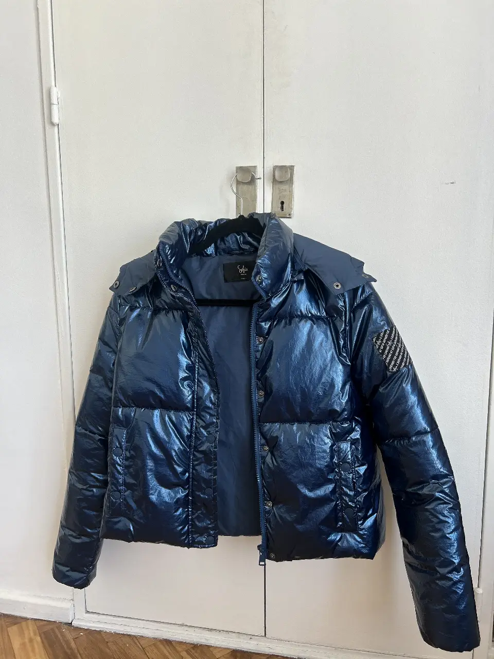 Campera puffer azul metalizado con capucha. Ideal para el invierno, con un diseño moderno y abrigo superior. Cuenta con cierre y etiqueta de la marca.