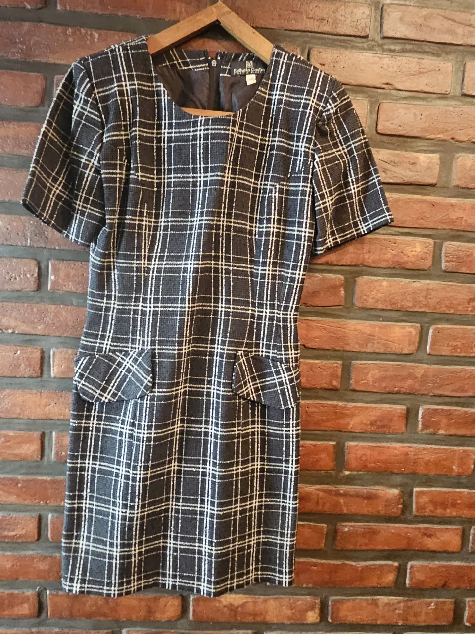 Vestido corto de manga corta con estampado a cuadros escoceses en tonos grises y blancos. Posee dos bolsillos plaqué en la parte delantera inferior.