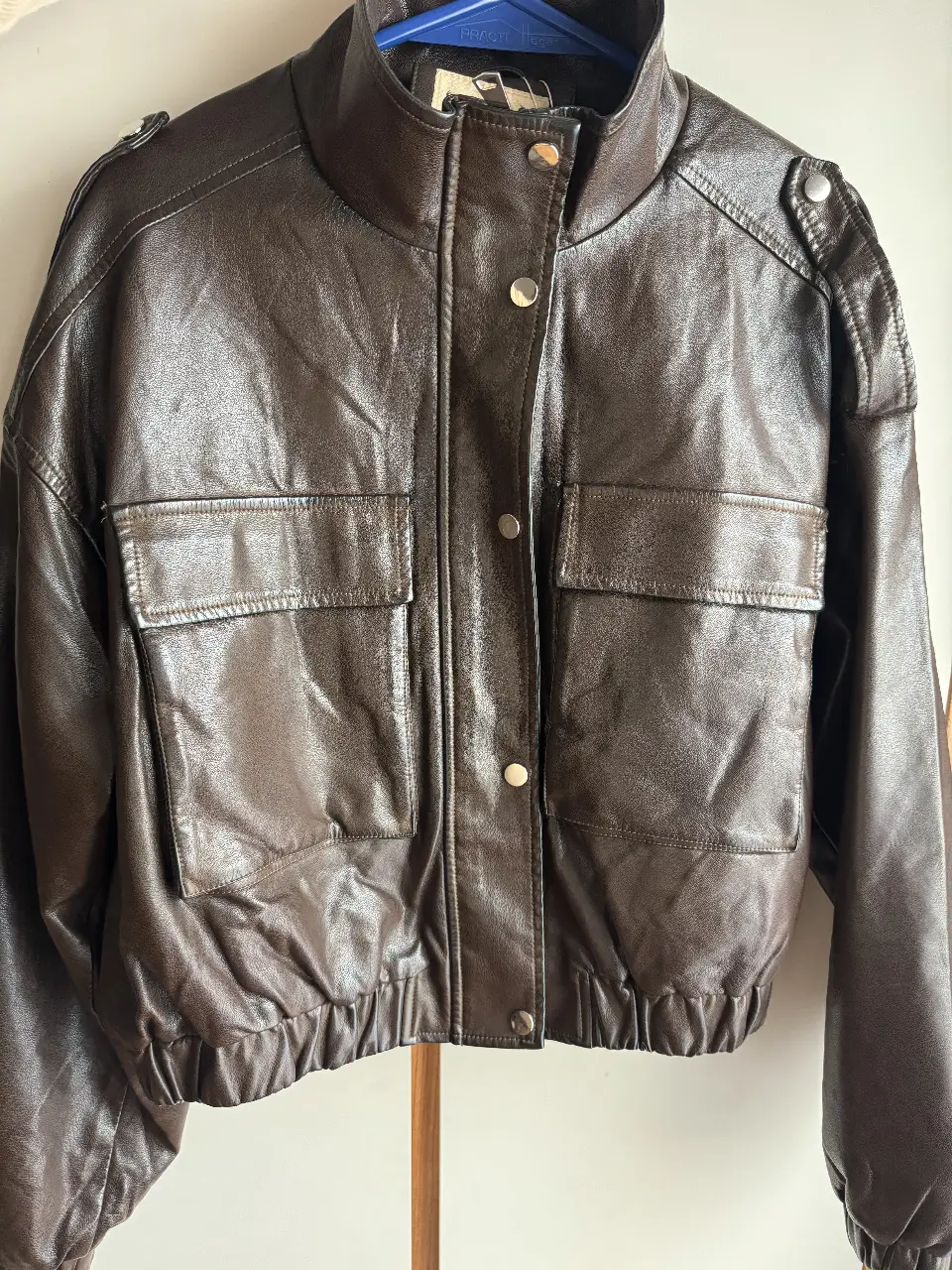 Chaqueta estilo biker de cuero sintético marrón. Posee dos bolsillos delanteros con solapa y cierre con botones a presión. Bolsillo interno, Cuello alto y detalles en los hombros. Ideal para un look casual y moderno.