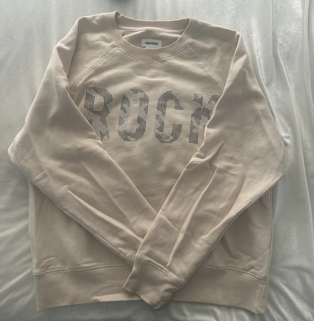 Buzo de  cuello redondo para mujer, color crudo con estampado "ROCK" con brillos. Ideal para un look casual y moderno.