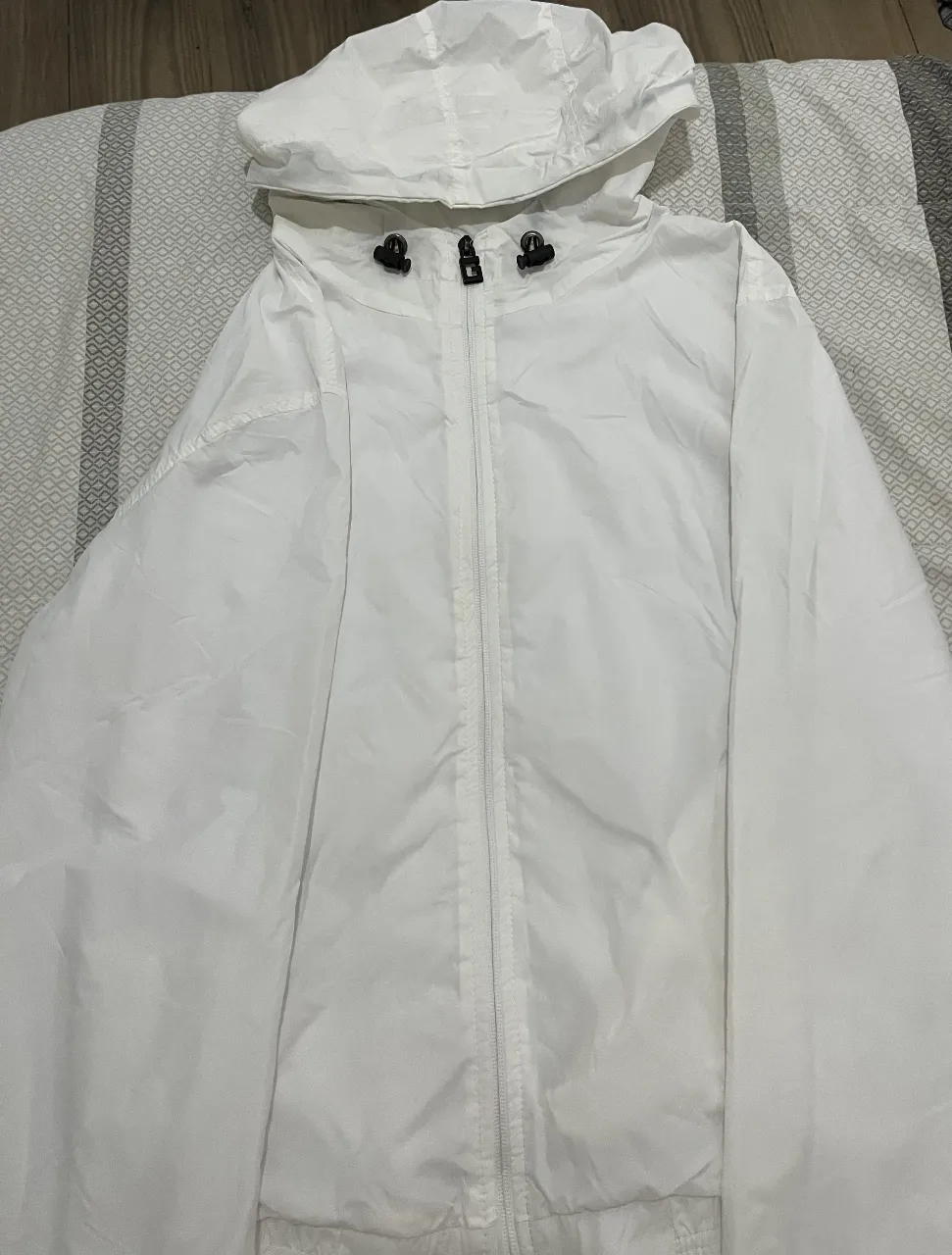 Rompevientos blanco con capucha y cierre frontal. Ideal para protegerte del viento y la lluvia ligera. Perfecto para un look casual y deportivo.