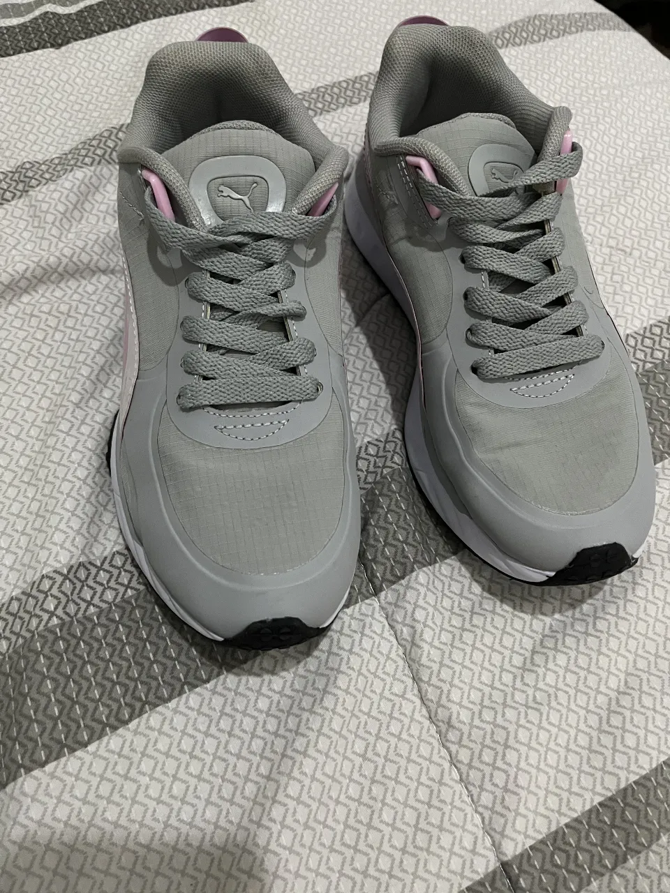 Zapatillas Puma grises con detalles en rosa y suela blanca. Ideales para running y uso diario. Diseño moderno y cómodo.