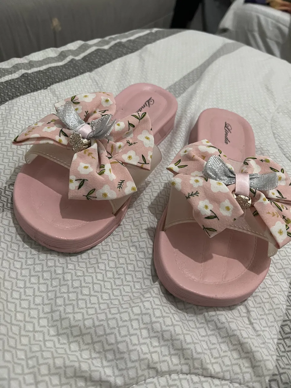 Lindas ojotas rosas con moño floreado y detalle plateado, ideales para un look fresco y femenino.