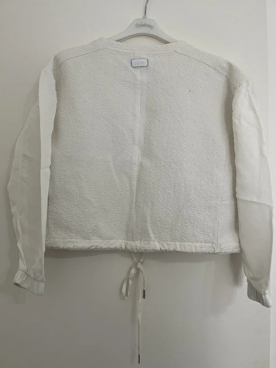 Buzo de cuello redondo blanco con detalles texturizados y ajuste en la cintura. Mangas amplias y detalles de diseño que le dan un toque moderno y versátil.
