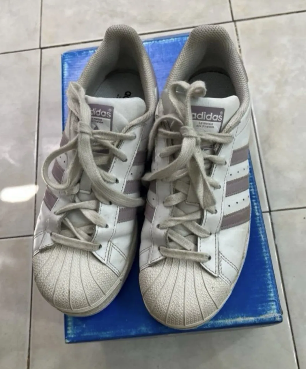 Zapatillas Adidas Superstar blancas con detalles en rosa pálido/lila. Un clásico que nunca pasa de moda, perfectas para el día a día. Ideales para darle un toque canchero a cualquier outfit.