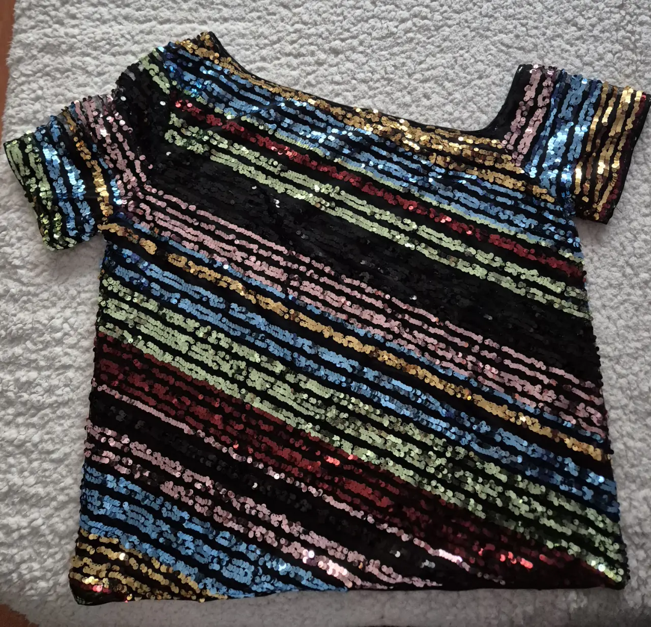 Top de fiesta con lentejuelas multicolores en diagonal. Diseño asimétrico con un hombro descubierto y mangas cortas. Ideal para eventos y salidas nocturnas.