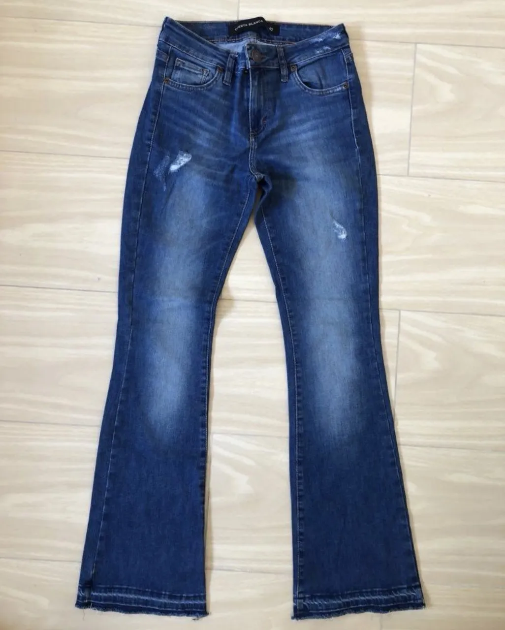 Jeans tiro alto estilo "flare" con un toque moderno. Tienen un lavado desgastado y detalles sutiles de roturas que le dan un aire vintage. 