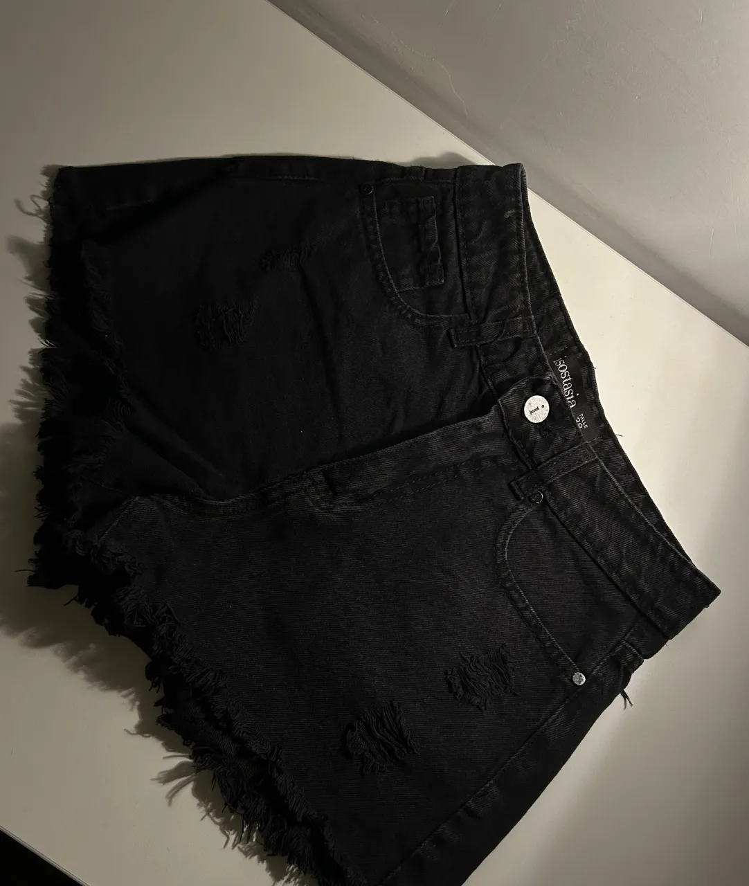 Short de jean negro tiro alto con roturas y detalles desflecados en los bordes. 
