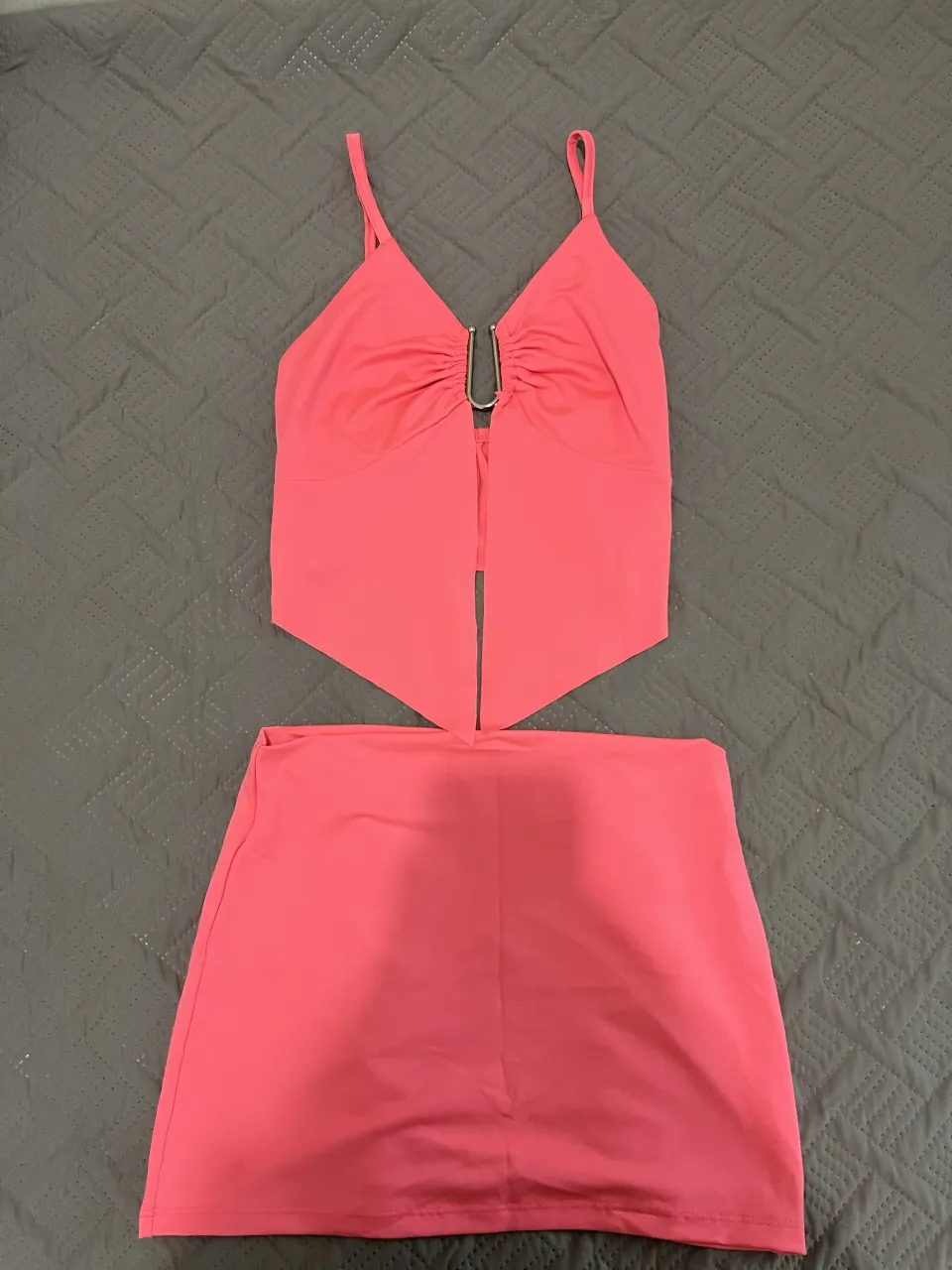 Conjunto súper canchero de top y pollera en color rosa vibrante. El top tiene breteles finos, escote en V y un detalle metálico con frunces en el busto. La pollera es tiro alto y recta. ¡Ideal para un look de verano o una salida nocturna!