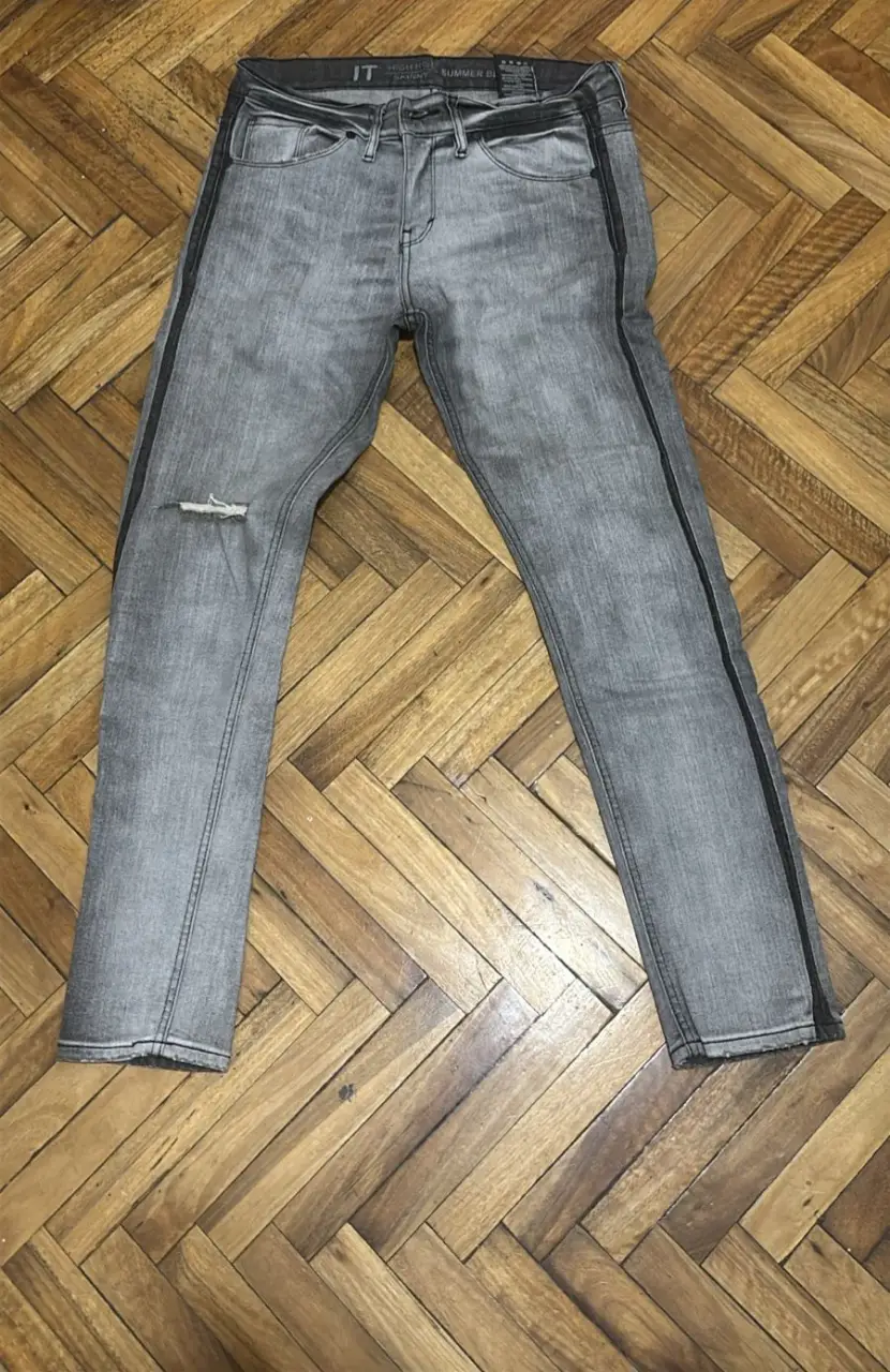 Jeans grises de hombre, tiro bajo, con detalle de rotura en la rodilla y línea negra lateral. Skinny, ideales para un look casual y moderno.