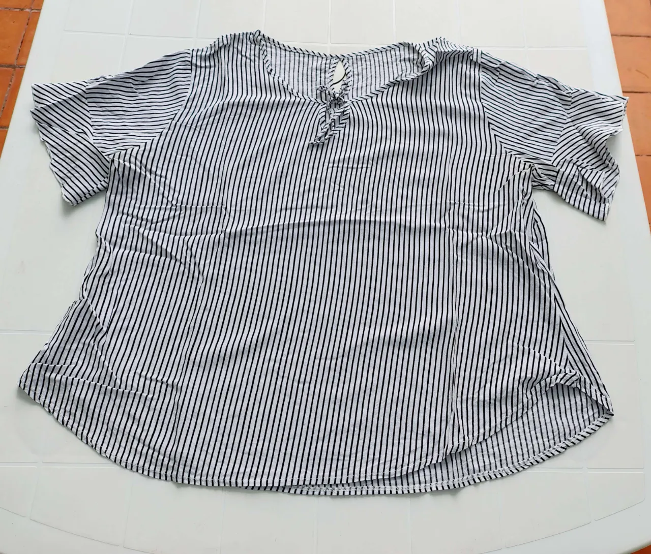 Remera a rayas verticales blancas y negras. Tiene un lazo en la parte delantera del cuello.